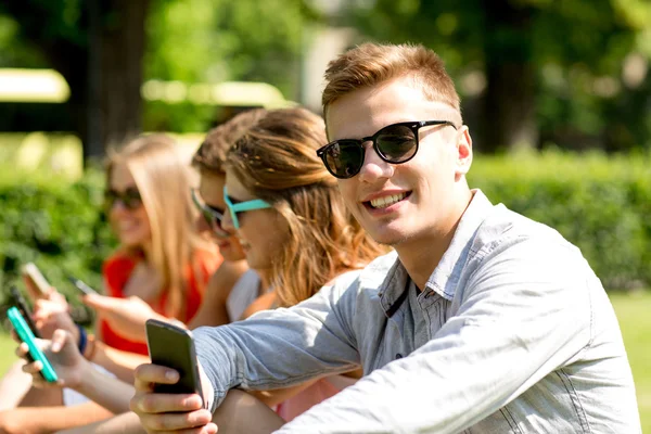 Lachende vrienden met smartphones zitten in park — Stockfoto