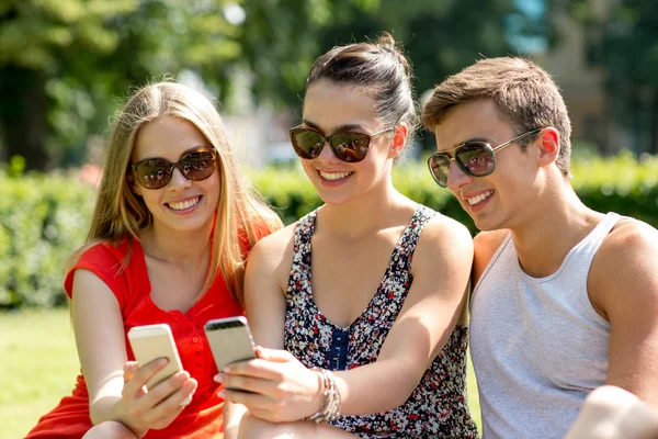 Amici sorridenti con gli smartphone seduti nel parco — Foto Stock