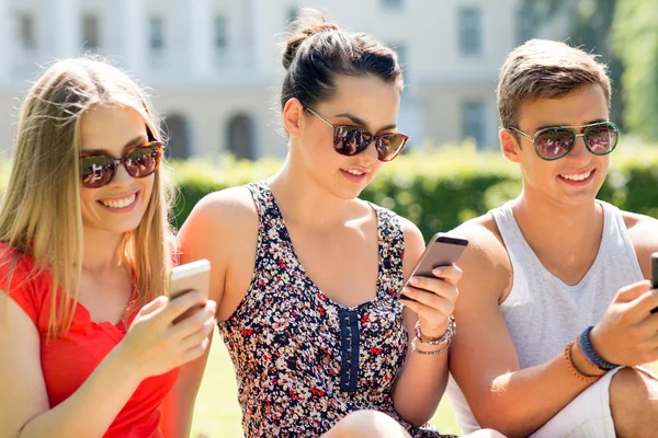 Amigos sonrientes con teléfonos inteligentes sentados en la hierba — Foto de Stock