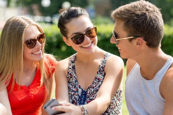 Smiling friends with smartphone sitting in park — Stock Photo, Image