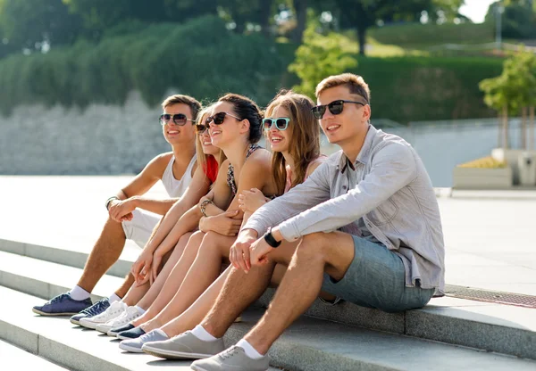Группа улыбающихся друзей сидящих на городской площади — стоковое фото