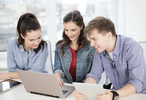 Tres estudiantes sonrientes con ordenador portátil y tableta PC — Foto de Stock