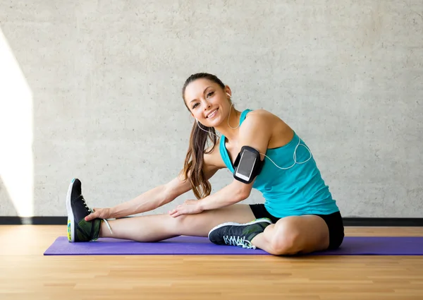 Mujer sonriente estirando la pierna en la estera en el gimnasio —  Fotos de Stock