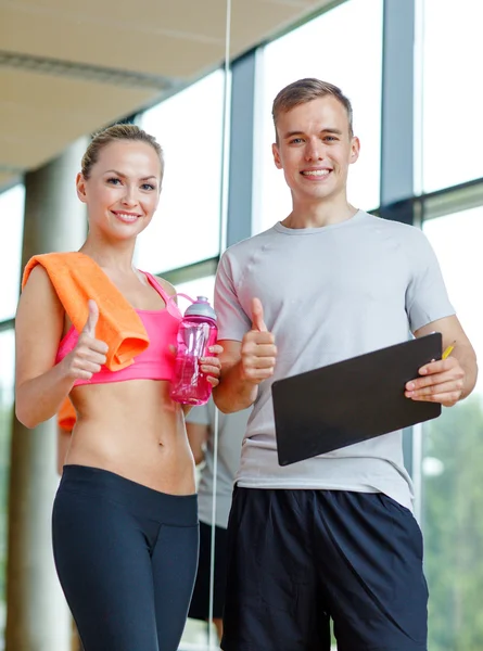 Smiling young woman with personal trainer in gym — Stock Photo, Image