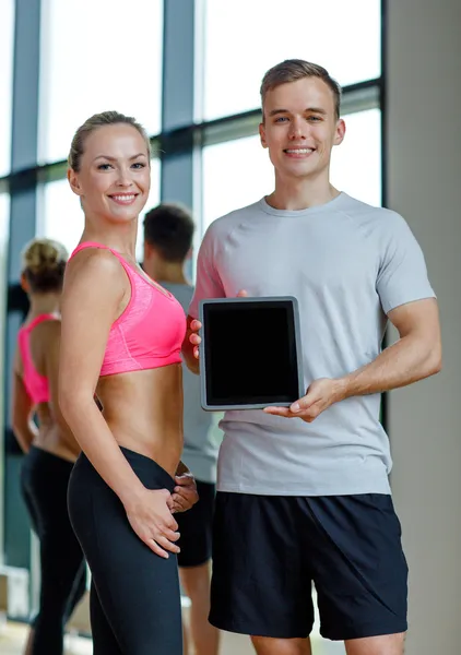 Smiling young woman with personal trainer in gym — Stock Photo, Image