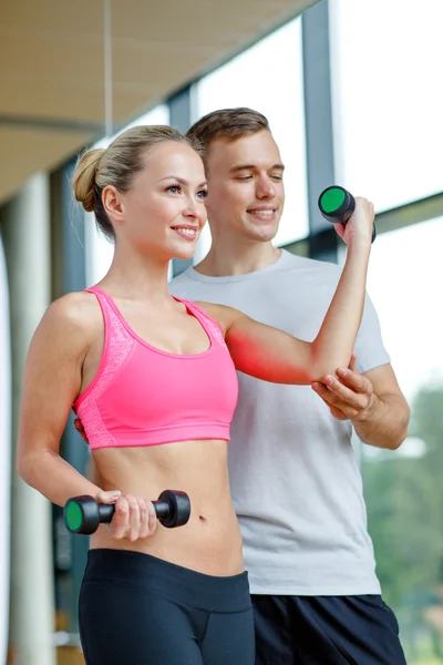 Giovane donna sorridente con personal trainer in palestra — Foto Stock