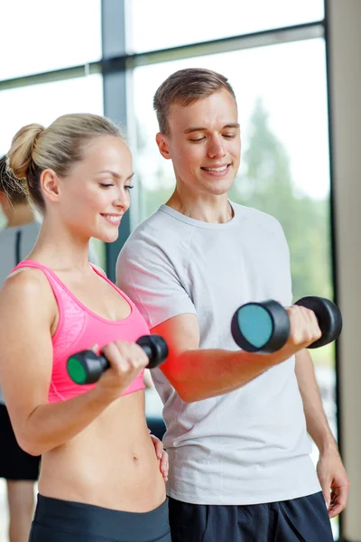 Smiling young woman with personal trainer in gym — Stock Photo, Image