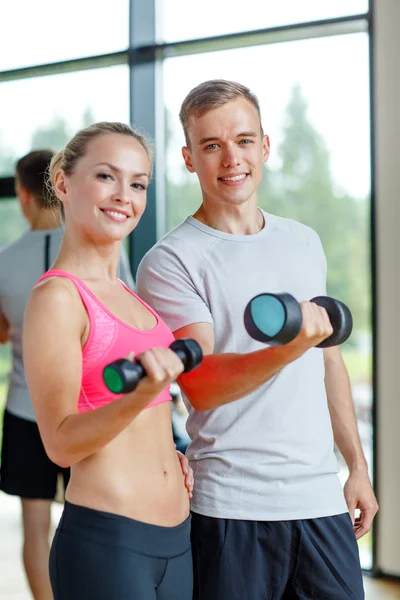 Leende ung kvinna med personlig tränare i gym — Stockfoto