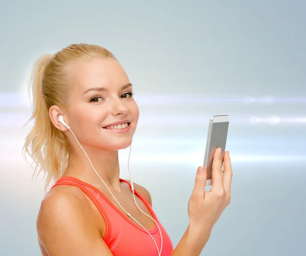 Улыбающаяся спортивная женщина со смартфоном и наушниками — стоковое фото