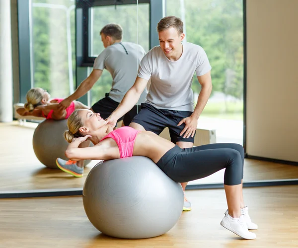 Smiling young woman with personal trainer in gym — Stock Photo, Image