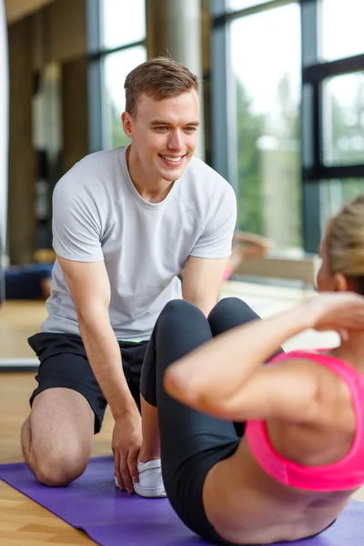 Mujer sonriente con entrenador masculino haciendo ejercicio en el gimnasio —  Fotos de Stock