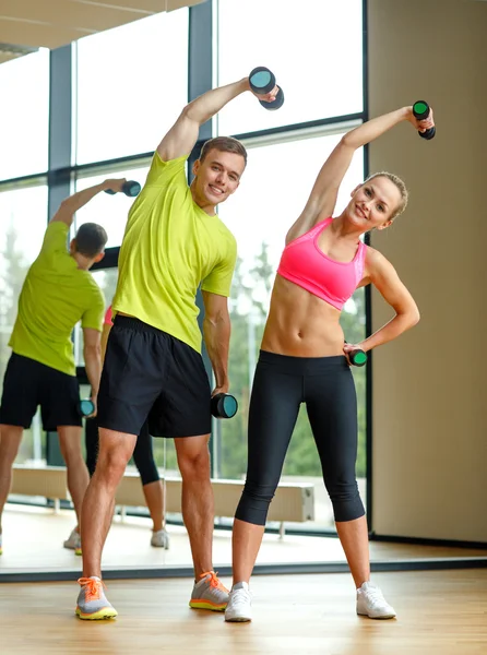 Homme et femme souriants avec haltères dans la salle de gym — Photo