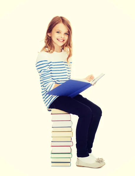 Little student girl sitting on stack of books — Stock Photo, Image