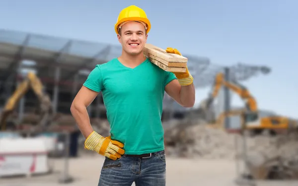 Ouvrier souriant dans un casque avec des planches en bois — Photo