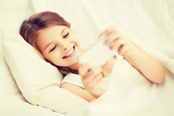 Kleines Mädchen mit Smartphone spielt im Bett — Stockfoto