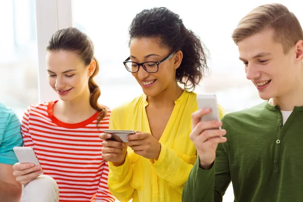 Tre leende studenter med smartphone i skolan — Stockfoto