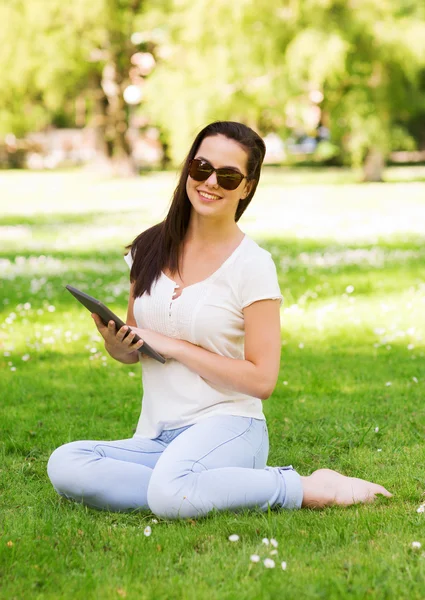 S úsměvem mladá dívka s tablet pc sedí na trávě — Stock fotografie