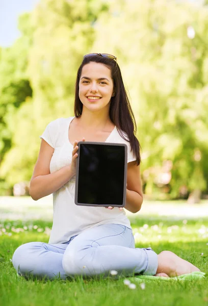 若い女の子の草の上に座ってタブレット pc に笑みを浮かべてください。 — ストック写真