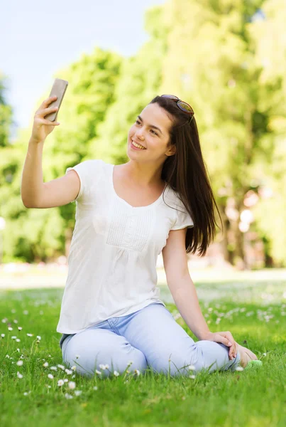 S úsměvem mladá dívka s smartphone sedí v parku — Stock fotografie