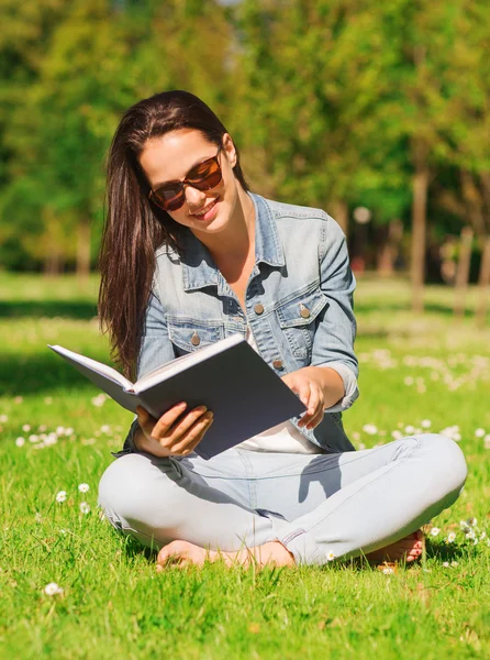 Sonriente joven con libro sentado en el parque — Foto de Stock