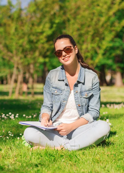 Sorridente ragazza con taccuino che scrive nel parco — Foto Stock