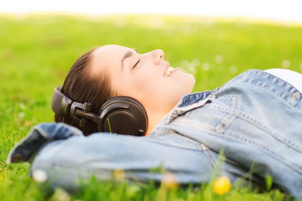 Sonriente chica joven en los auriculares acostado en la hierba — Foto de Stock