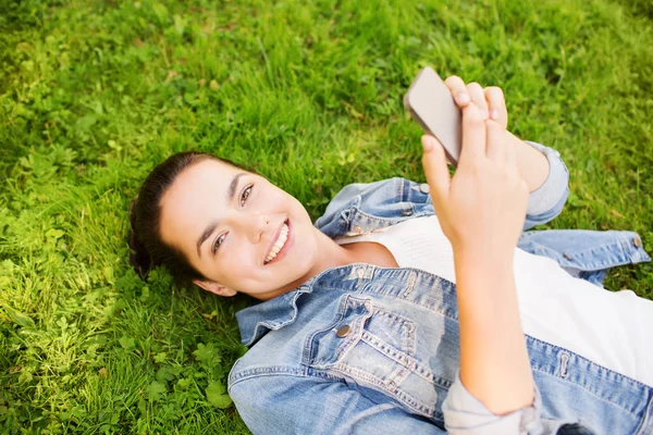 Glimlachend jong meisje met smartphone liggen op gras — Stockfoto