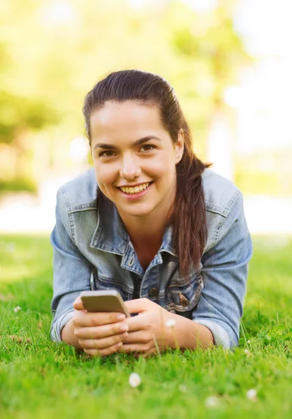 Улыбающаяся молодая девушка со смартфоном, лежащим на траве — стоковое фото