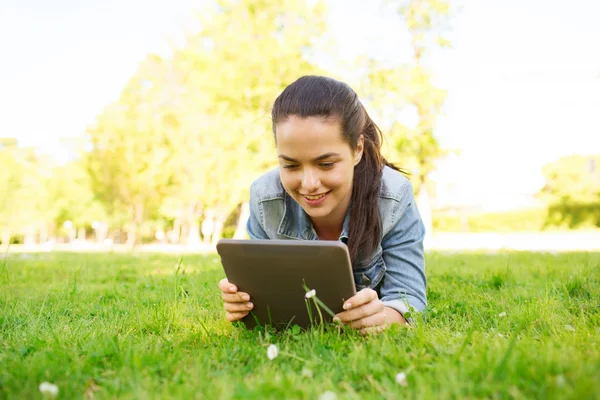 Sonriente chica joven tableta pc acostado en la hierba — Foto de Stock