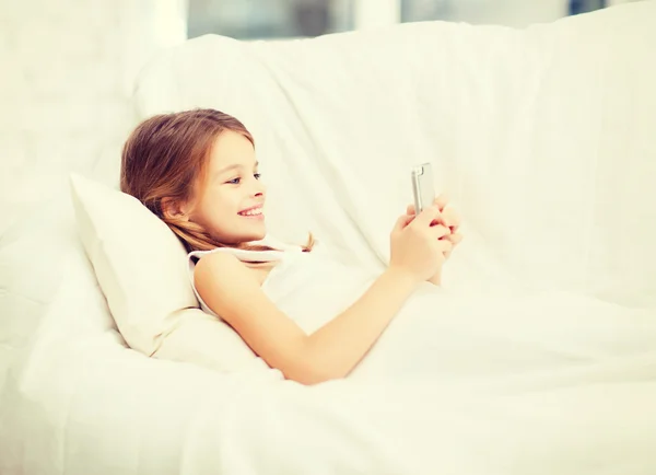 Liten flicka med smartphone spelar i sängen — Stockfoto