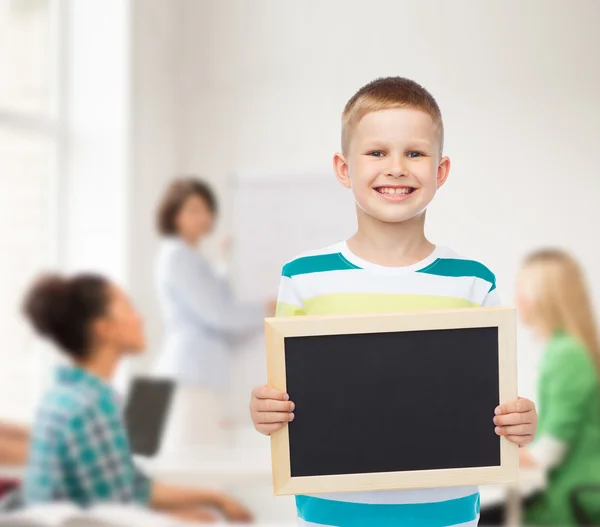 Smiling little boy holding blank black chalkboard — Stock Photo, Image