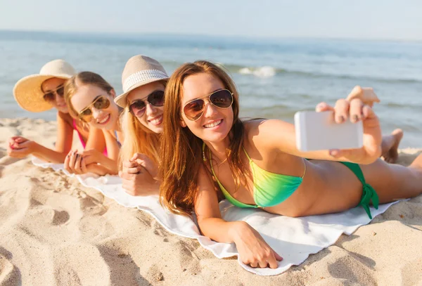 Группа улыбающихся женщин со смартфоном на пляже — стоковое фото