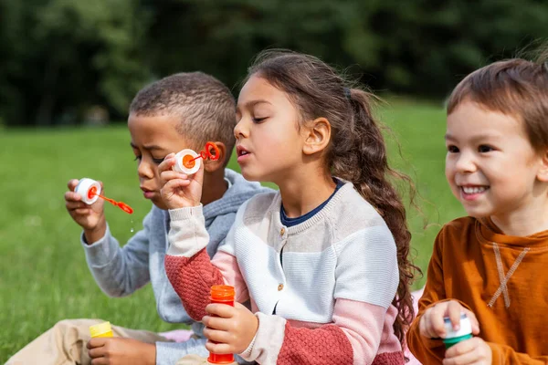 Группа детей, раздувающих мыльные пузыри в парке — стоковое фото