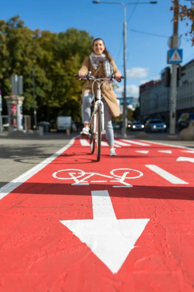 woman cycling along red bike lane road in city