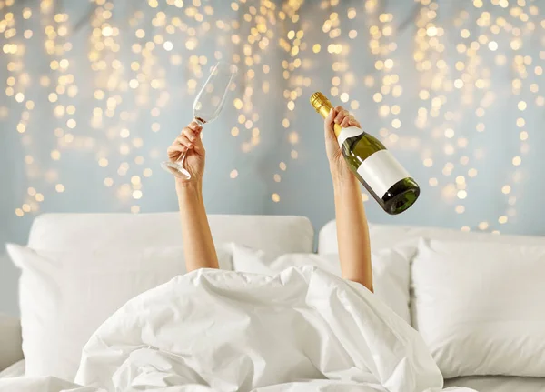 躺在床上喝香槟的女人的手 图库图片