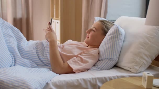 Happy girl with smartphone in bed at home — Stock Video