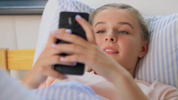 Щаслива дівчина зі смартфоном в ліжку вдома — стокове відео
