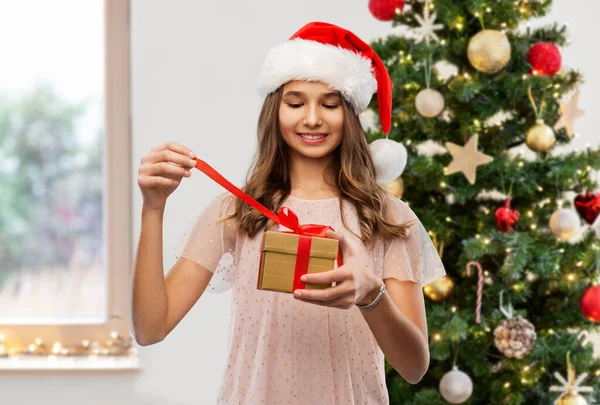 Dospívající dívka v Santa klobouk otevření vánoční dárek — Stock fotografie