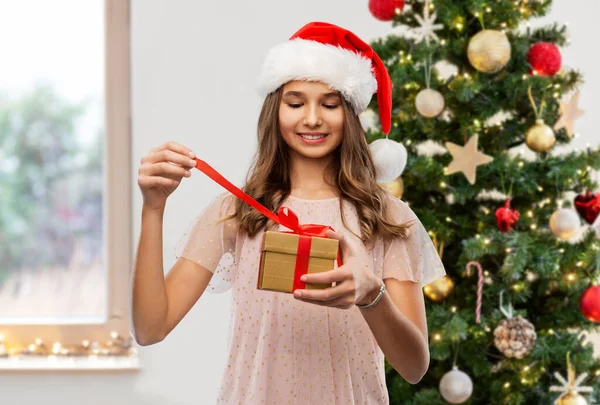 Tiener meisje in santa hoed opening kerstcadeau — Stockfoto