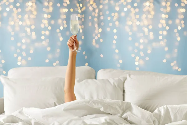 Hand kvinna liggande i sängen med champagneglas — Stockfoto