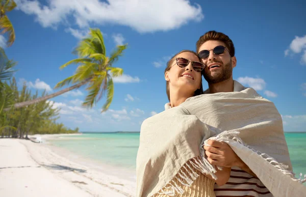 Lyckligt par täckt med filt kramas på stranden — Stockfoto