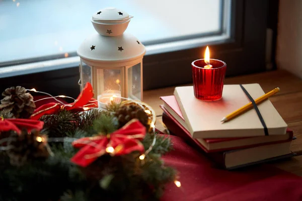 Grinalda de Natal, livros, vela, lanterna na janela — Fotografia de Stock