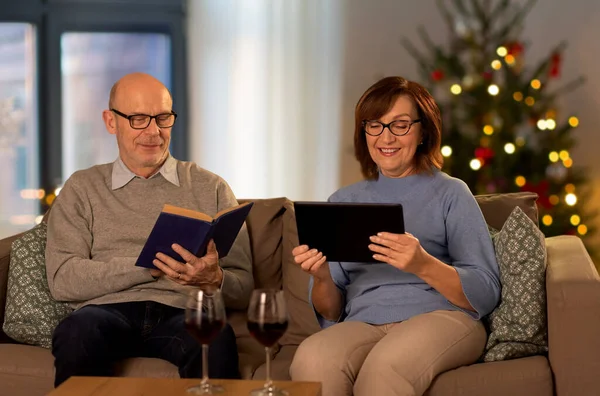 Ηλικιωμένο ζευγάρι με το βιβλίο και το tablet PC στο σπίτι — Φωτογραφία Αρχείου