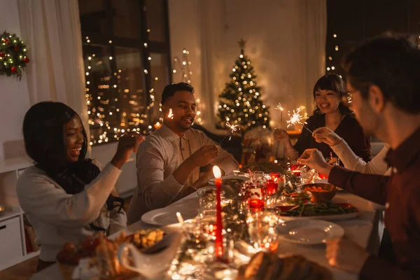 Amigos felices con bengalas en la cena de Navidad —  Fotos de Stock