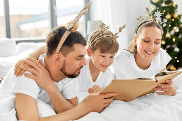 Οικογένεια με βιβλίο με πιτζάμες στο κρεβάτι τα Χριστούγεννα — Φωτογραφία Αρχείου