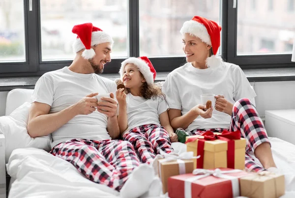 Mutlu aile Noel 'de yatakta kurabiye yiyor. — Stok fotoğraf
