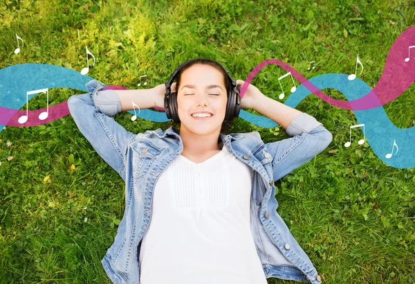 Sorrindo menina em fones de ouvido deitado na grama — Fotografia de Stock
