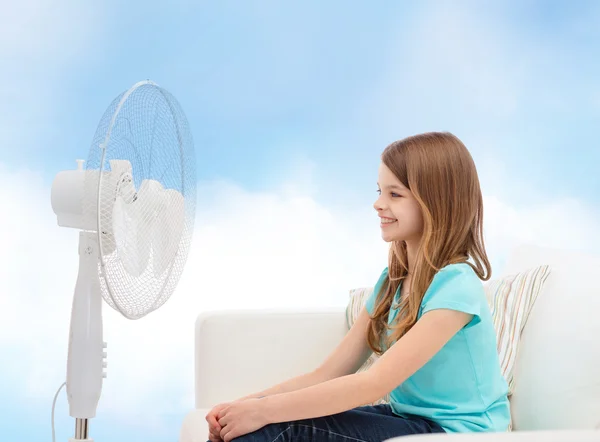 Petite fille souriante avec un grand ventilateur à la maison — Photo