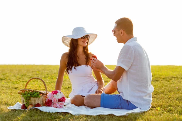 Sonriente pareja con pequeña caja de regalo roja en el picnic —  Fotos de Stock