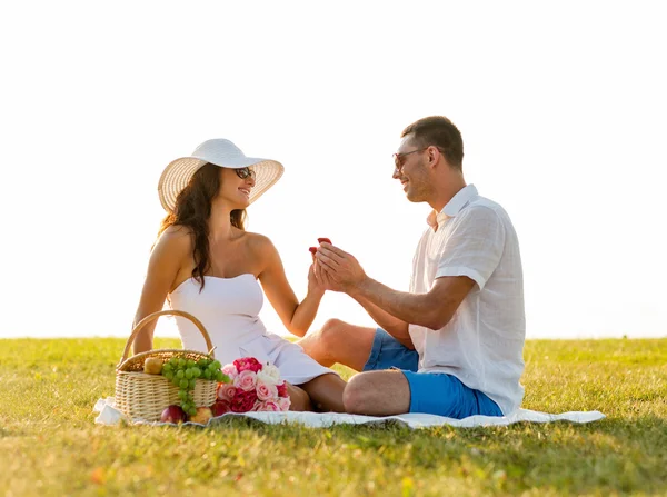 Sonriente pareja con pequeña caja de regalo roja en el picnic —  Fotos de Stock